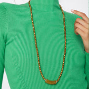 Woman's bust wearing a green blouse and a long gold tone necklace with acrylic focal bead