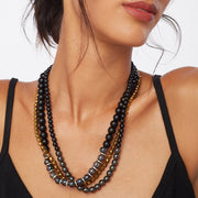 Brunette wearing a three strand necklace with magnetic clasp in silver, gold and black tones incorporating black onyx, plated hematite and signature Greek ceramic beads.