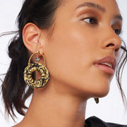 Brunette wearing a pair of front facing hand crocheted statement hoops hanging from horseshoe-shaped earring posts in gold tones with a crystal cut glass in silver tones in the center.