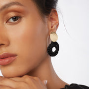 Brunette wearing a small pair of front facing hoops in black with oval gold tone earring posts.