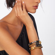 Photo of brunette wearing a set of 4 bracelets in mixed metal, brown and black tones with gemstones and a horn-like acrylic focal bead.