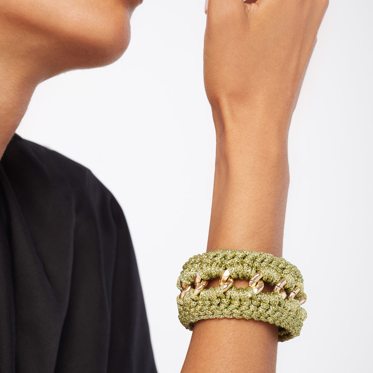 Woman with black blouse wears chunky  hand crocheted bracelet where gold tone chain meets olive green and gold tones.