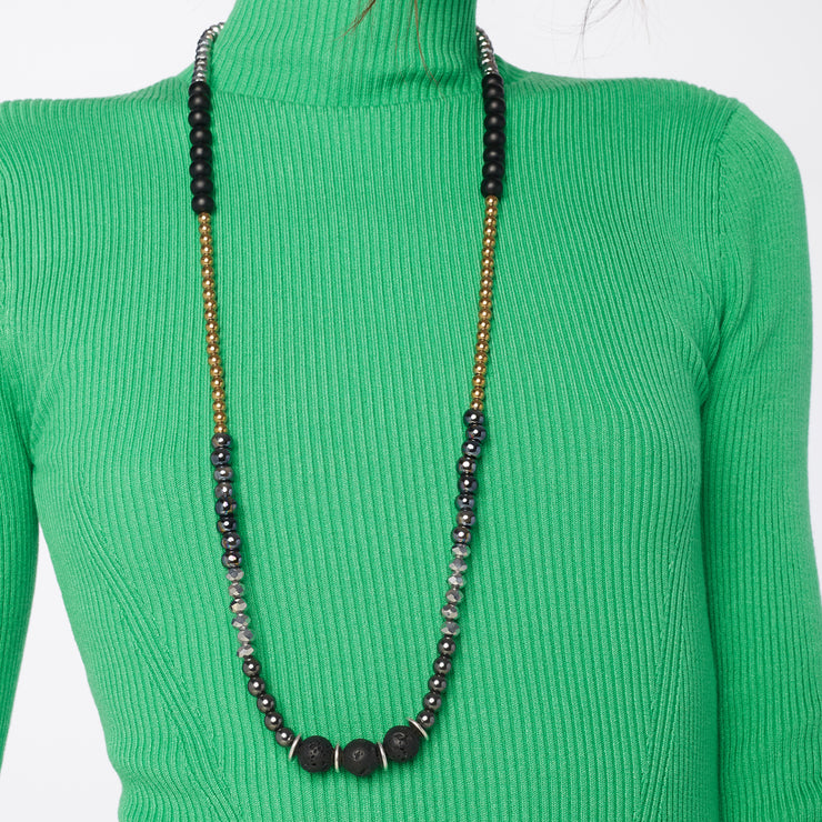 Woman in green blouse wearing a long black and gold necklace with chunky black lava and smaller gold tone hematite  gemstones