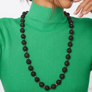 Girl in green blouse wearing a long black and gold necklace with chunky black lava and smaller gold tone hematite  gemstones