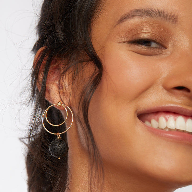 Smiling brunette wearing a pair of front facing double hoop earrings with inner and outer circle and a black lava dangle.