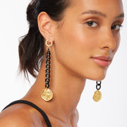 Brunette wearing a pair of very long earrings with distressed black chain, Greek coin charm in gold and gold tone wreath style posts.