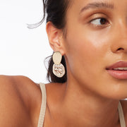 Brunette wearing a pair of earrings with oval gold plated earring posts and silver plated Greek coins.